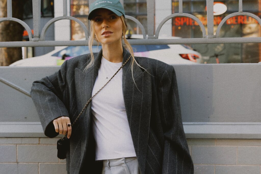Modelka w czarnej marynarce oversize i czapce z daszkiem prezentuje minimalistyczny naszyjnik PARTS JEWELRY podczas sesji modowej w Berlinie.