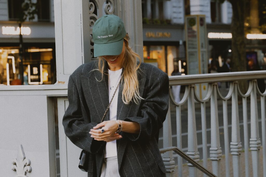 Modelka w czarnej marynarce oversize i zielonej czapce prezentuje autorską biżuterię PARTS JEWELRY podczas miejskiej sesji zdjęciowej w Berlinie.